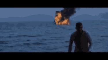 a man is standing in front of a burning ship in the ocean