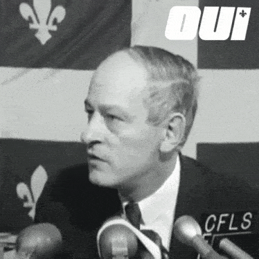 a man in a suit and tie is speaking into a microphone with the word oui behind him