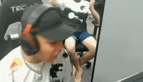 a man wearing a red bull shirt is sitting in front of a computer monitor .