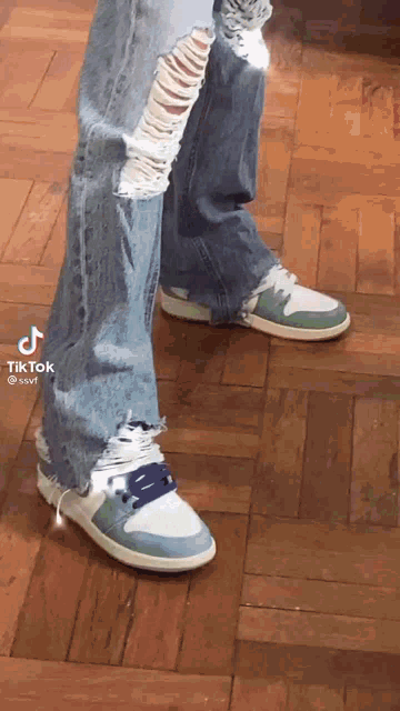 a person wearing ripped jeans and a pair of sneakers on a wooden floor .