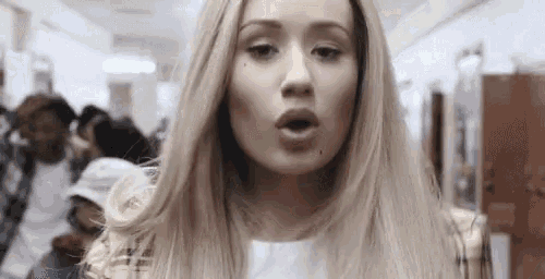 a woman with blonde hair is standing in a hallway with her mouth open and a crowd of people behind her .