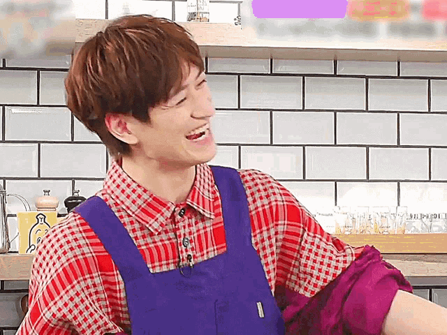 a man wearing a plaid shirt and a blue apron is laughing in a kitchen