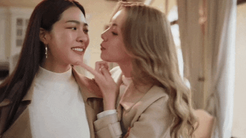 two women are touching each other 's faces and smiling .