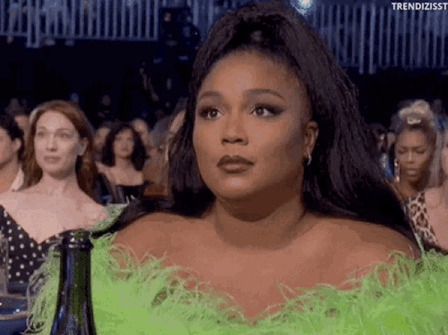 a woman in a green feathered dress is sitting in front of a crowd of people .