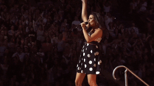 a woman in a black and white polka dot dress is singing into a microphone
