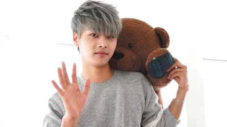 a young man in a grey sweater is holding a teddy bear