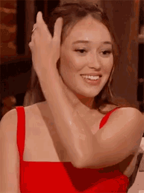 a woman in a red dress is smiling and making a peace sign .