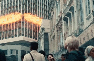 a group of people are walking down a street in front of a burning building .