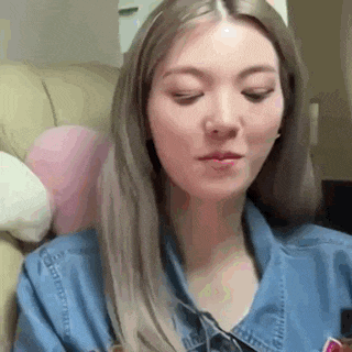 a woman is sitting on a couch with her eyes closed and wearing a denim shirt .