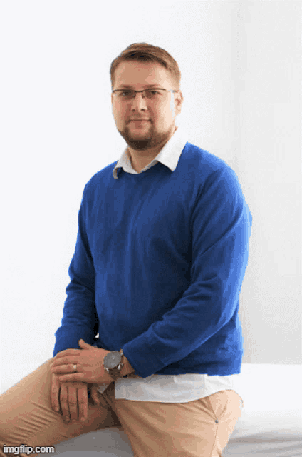 a man in a blue sweater sits with his hands folded