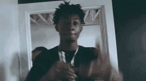 a young man is standing in front of a door holding a gun and making a funny face .