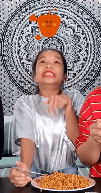 a young girl is sitting at a table eating noodles with a fork .
