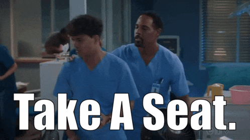 two men in scrubs are walking with the words take a seat