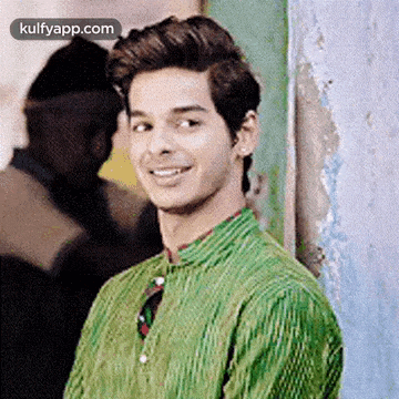 a young man in a green shirt is smiling in front of a wall .