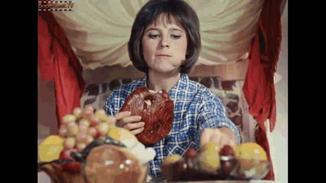 a woman in a plaid shirt is eating a piece of meat next to a bowl of fruit