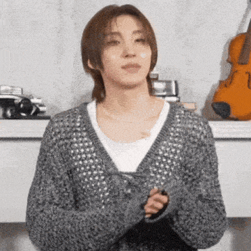 a woman wearing a grey sweater is standing in front of a violin .