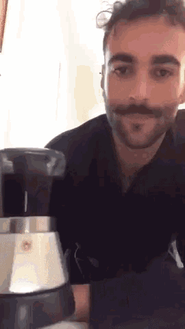 a man with a mustache is sitting at a table with a coffee maker