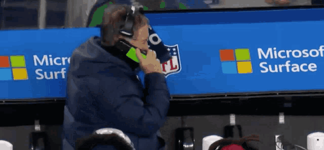 a man is talking on a cell phone in front of a microsoft surface sign