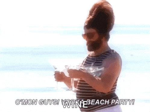 a man with a beard is holding a glass of wine on a beach .