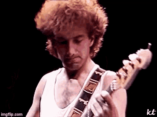 a man in a white tank top is playing a bass guitar on a stage .