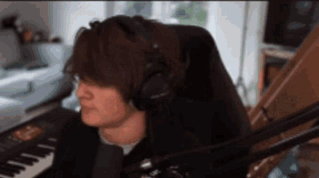 a man wearing headphones is sitting in front of a microphone and a piano .