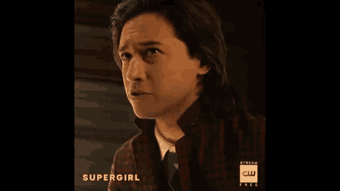 a man with long hair is wearing a plaid shirt and tie with the words supergirl on the bottom