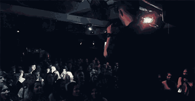 a crowd of people are gathered in a dark room watching a performance