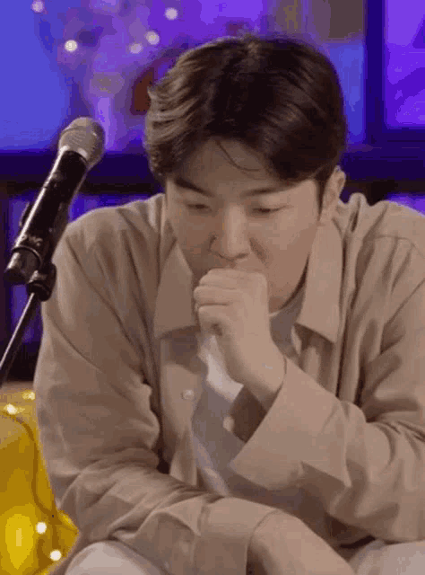 a young man is sitting in front of a microphone and covering his mouth with his hand .