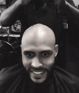 a bald man with a beard is getting his hair cut in a barber shop .