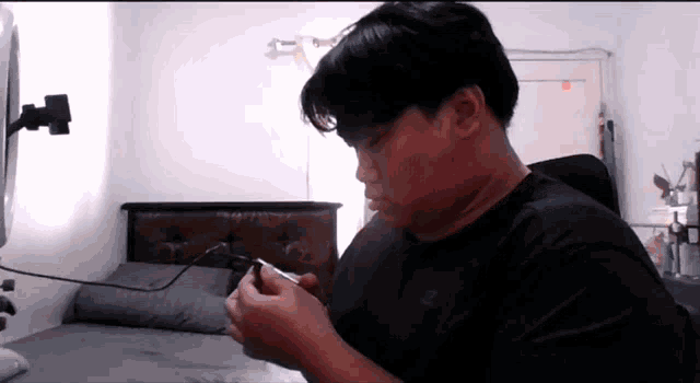 a man in a black shirt is smoking a cigarette in a bedroom .