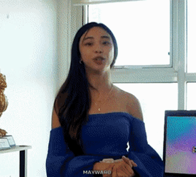 a woman wearing a blue off the shoulder top is standing in front of a window ..