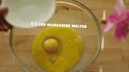 a person is pouring milk into a bowl with eggs and butter .