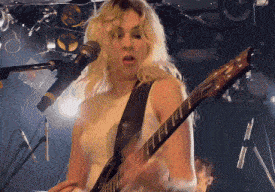 a blonde woman is playing a guitar in front of a microphone