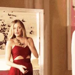 a woman in a red dress is standing in front of a mirror and looking at herself .