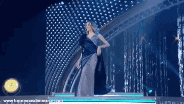 a woman in a blue dress stands on a stage with the website www.fororeinasdemexico.com in the lower right corner