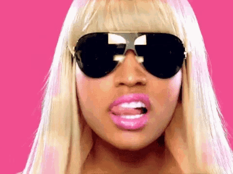 a woman wearing sunglasses and pink lipstick sticking out her tongue
