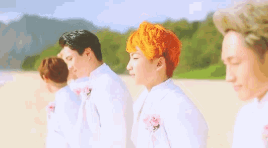a group of men with orange hair are standing on a sandy beach .