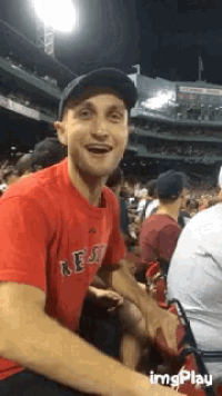 a man wearing a red shirt that says boston is sitting in a stadium