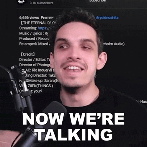 a man in front of a microphone with the words now we 're talking behind him