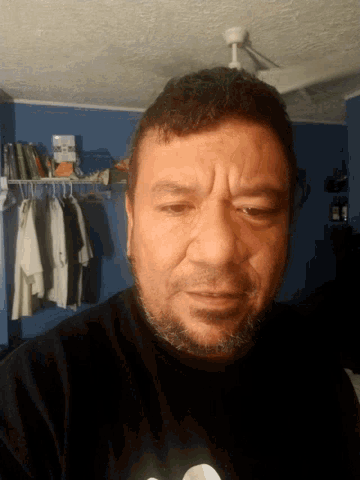a man with a beard and a black shirt has his eyes closed in front of a closet