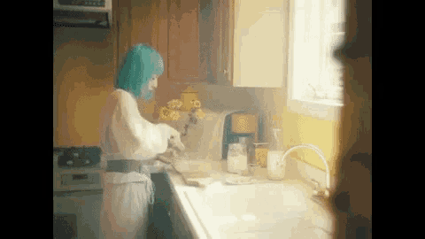 a woman with blue hair is standing in a kitchen preparing food