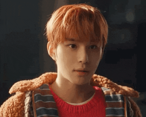 a close up of a young man with red hair wearing a red sweater and a brown jacket .