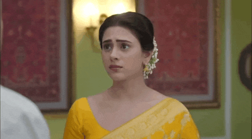 a woman in a yellow saree is looking at the camera