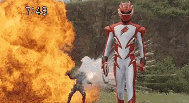 a man in a red and white superhero costume is standing in front of a large explosion .
