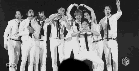 a group of men in white shirts and ties are standing next to each other on a stage making hearts with their hands .