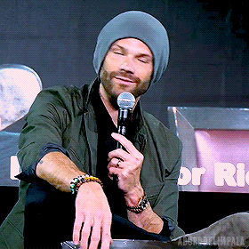 a man wearing a beanie holds a microphone in front of a sign that says rio