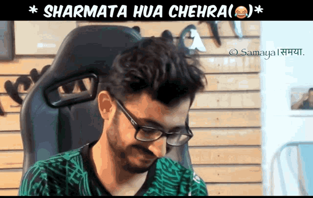 a man wearing glasses sits in a chair with the words sharmata hua chehra