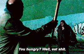 a man is holding a stick in his hand while another man says `` you hungry ? well eat shit . ''