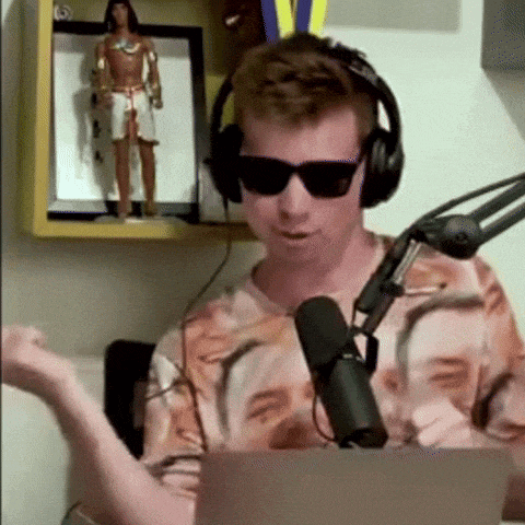 a man wearing headphones and sunglasses is sitting in front of a microphone and a laptop .