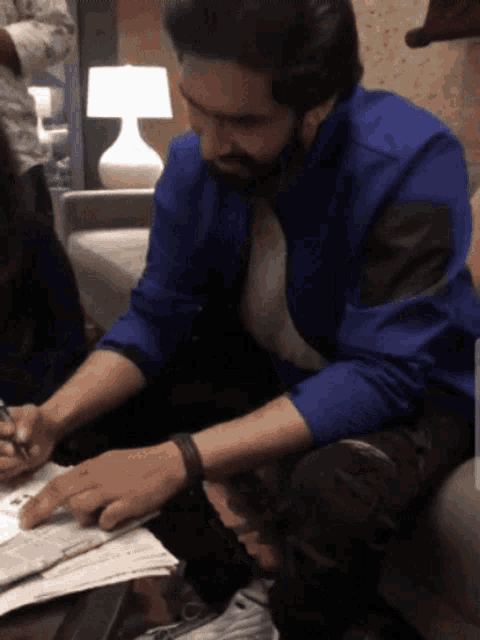 a man in a blue shirt sits on a couch looking at a piece of paper